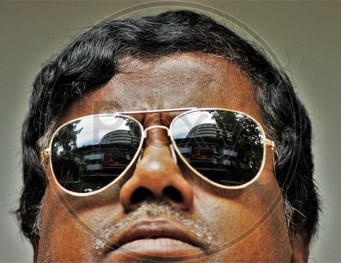 The Bombay Stock Exchange (BSE) building is reflected in the glasses of a man as he watches the Sensex results following the coronavirus outbreak, on the large screen outside the facade of the building in Mumbai, March 12, 2020.