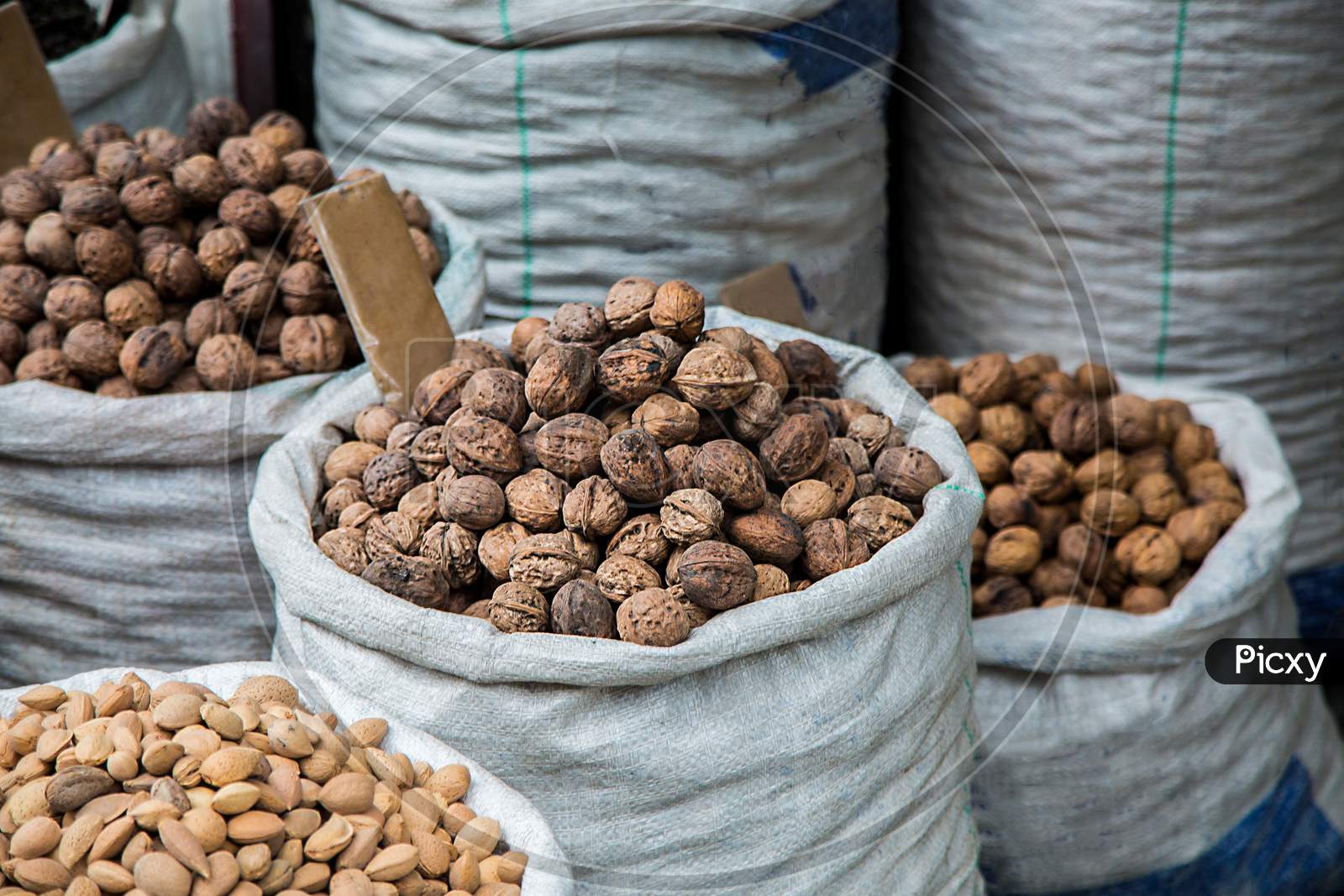 Walnuts And Pistachios For Sale At Market In White Sacks , Variety Of Dry Fruits Displayed Outside The Shop - Image