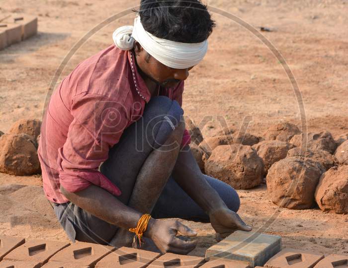 TIKAMGARH, MADHYA PRADESH, INDIA - FEBRUARY 07, 2020: Unidentified Indian man making house bricks by hand using a mold and wet clay.