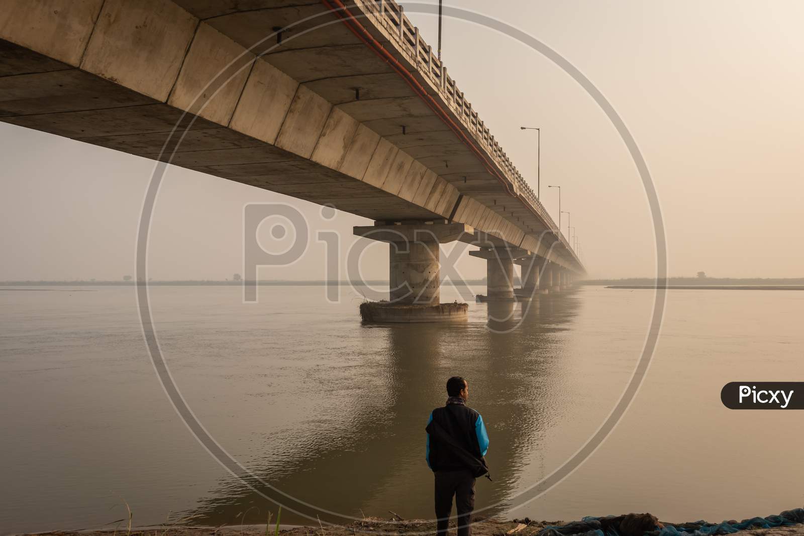Man Watching Road Bridge Over River With Its Water Reflection At Dawn