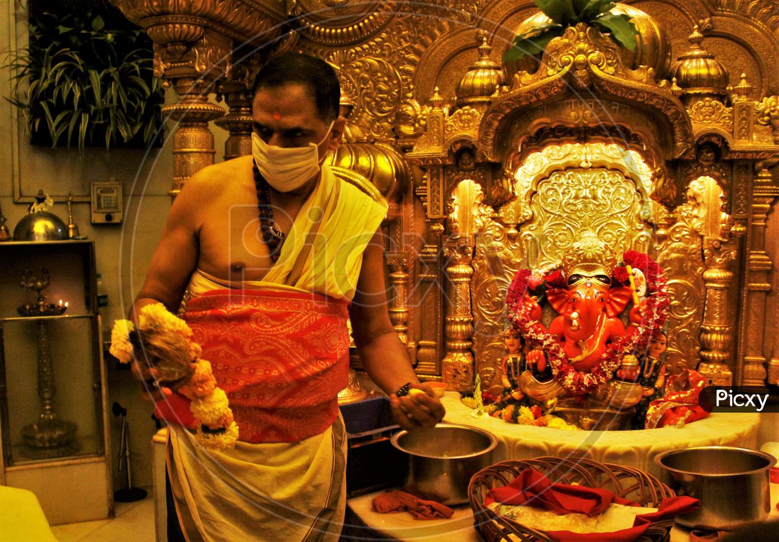A Hindu priest wearing a facemask amid concerns over the spread of the COVID-19, is seen standing next to an idol of Lord Ganesha, at a temple in Mumbai on March 13, 2020.