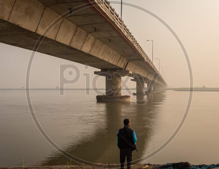 Man Watching Road Bridge Over River With Its Water Reflection At Dawn