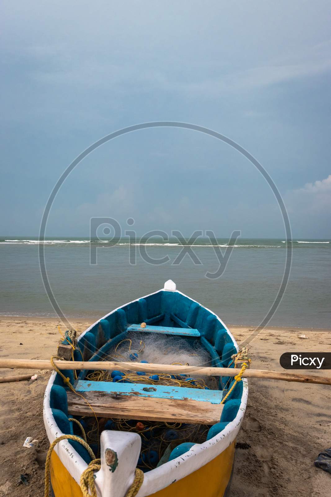Fishing Boat With Fishing Net On The Yellow Sandy Beach With Clouds And Blue Sky