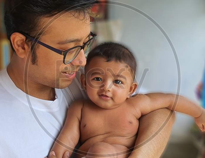 A Smiling Little Baby Boy Held By His Father With Blurred Background
