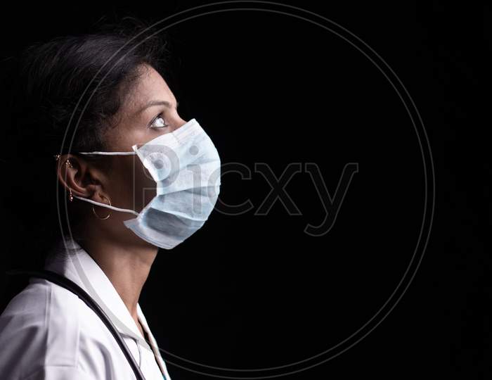 Profile View Of Young Woman Doctor With Opened Eyes In Medical Mask On Black Background Looking Up - Concept Of Hope And Fight To End Coronavirus Or Covid-19 Crisis.