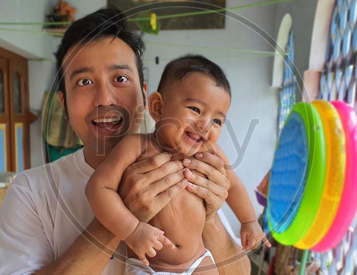 A Smiling Little Baby Boy Held By His Father With Blurred Background