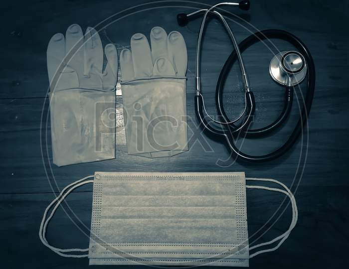 A Pair Of Rubber Medical Gloves, Surgical Mask And Black Stethoscope On A Wooden Table.