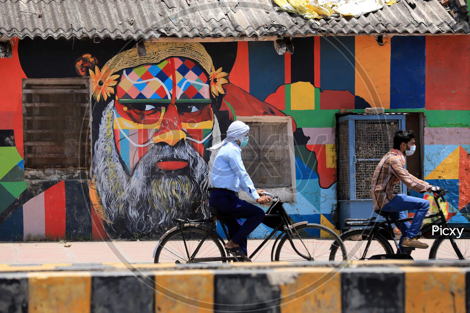 Men ride past a mural On A Hot Weather day In Prayagraj, May 26, 2020.