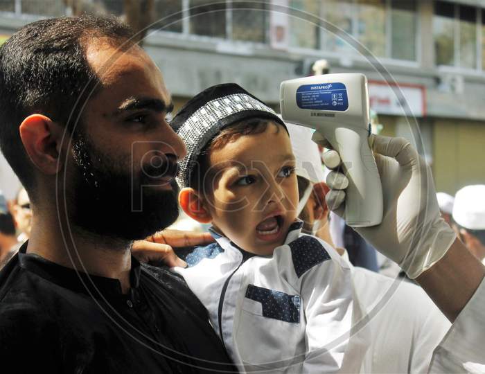 A kid reacts upon a devotee getting scanned with an infrared thermometer to check his temperature as a precautionary measure against coronavirus outside a mosque in Mumbai, India, March 20, 2020.