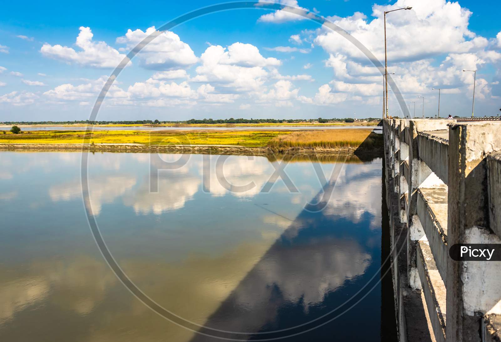 Clear Blue Sky With Many Small Cloud Patch And River Water Reflection By The Side Of River Bridge