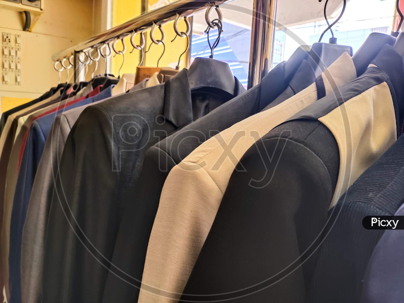 Men multi colored blazers hanging inside a shop .Closeup of gray man's suit with others hanging on hangers in tailor shop.Shop jacket men series, business hanger clothing. blazers for Men in wedding