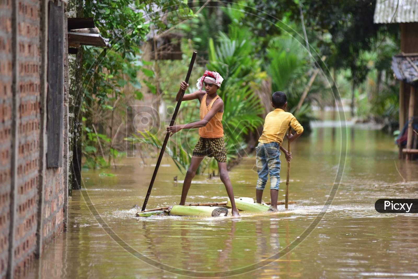 Boys Row A Makeshift Raft Past Submerged Houses At A Flood-Affected  Bakulguri Village Near Kampur In Nagaon District Of Assam On May 27,2020.