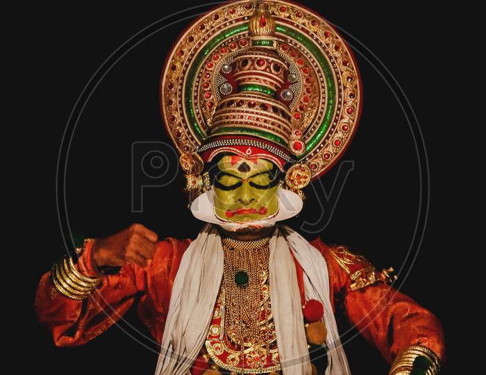 A Kathakali Dancer Dancing On A Black Background With Spotlight On His Face.