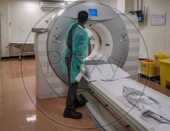 Computed Tomography machine (CT) in Radiology Department with radiology technician wearing personal protective equipment (PPE) disinfecting it
