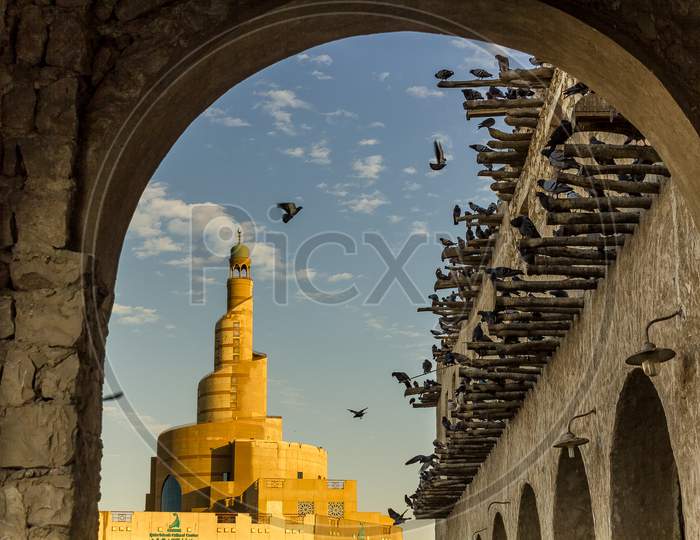 Al-Fanar Qatar Islamic Cultural Center daylight exterior view with pigeons flying in the sky in foreground and clouds in sky in background