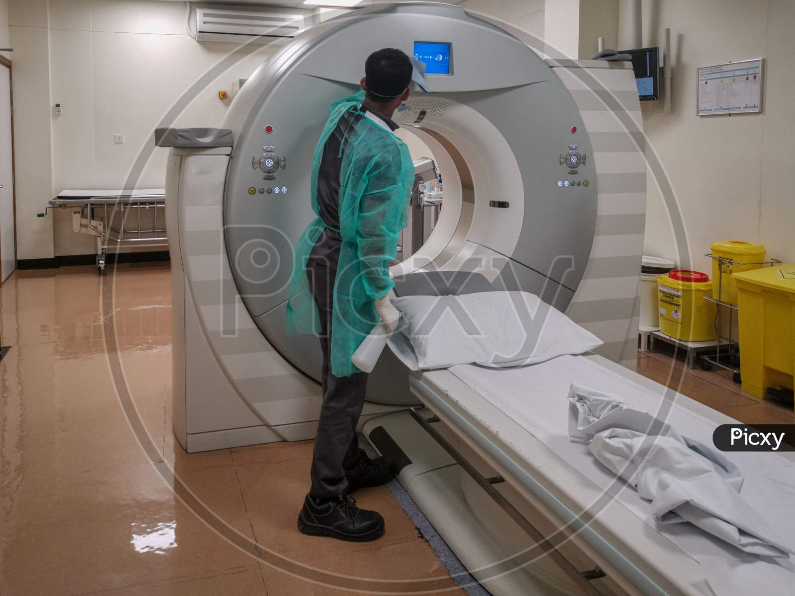 Computed Tomography machine (CT) in Radiology Department with radiology technician wearing personal protective equipment (PPE) disinfecting it
