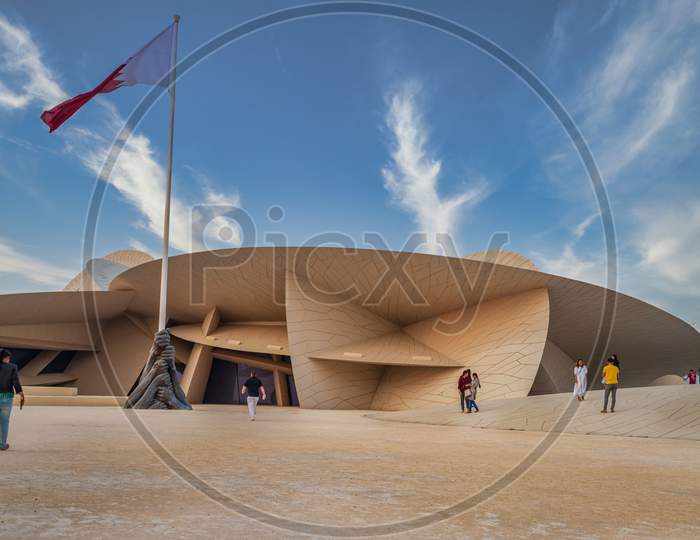 National Museum of Qatar (Desert rose) exterior  daylight view with  Qatar flag and clouds in sky