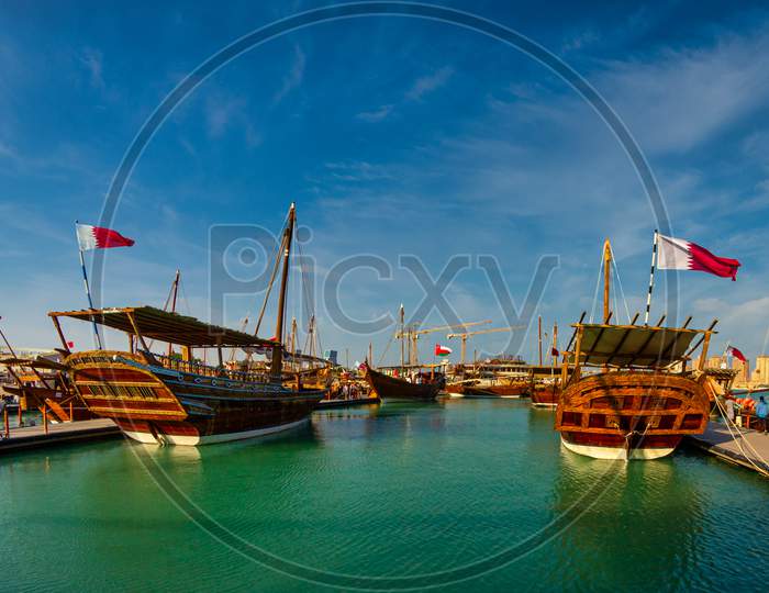 Traditional wooden boats (dhows) in Katara beach Qatar daylight view with Qatar flag and clouds in sky