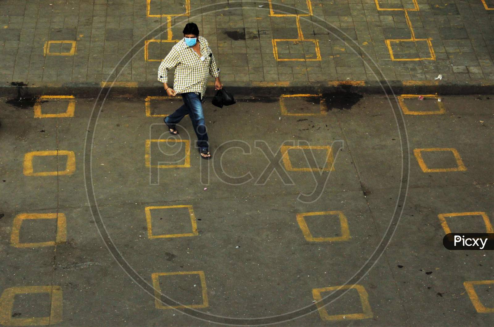 A man wearing protective mask walks on the squares painted by the BMC for maintaining physical distance at a market place to limit the spread of the coronavirus disease (COVID-19), in Mumbai, India on March 28, 2020.