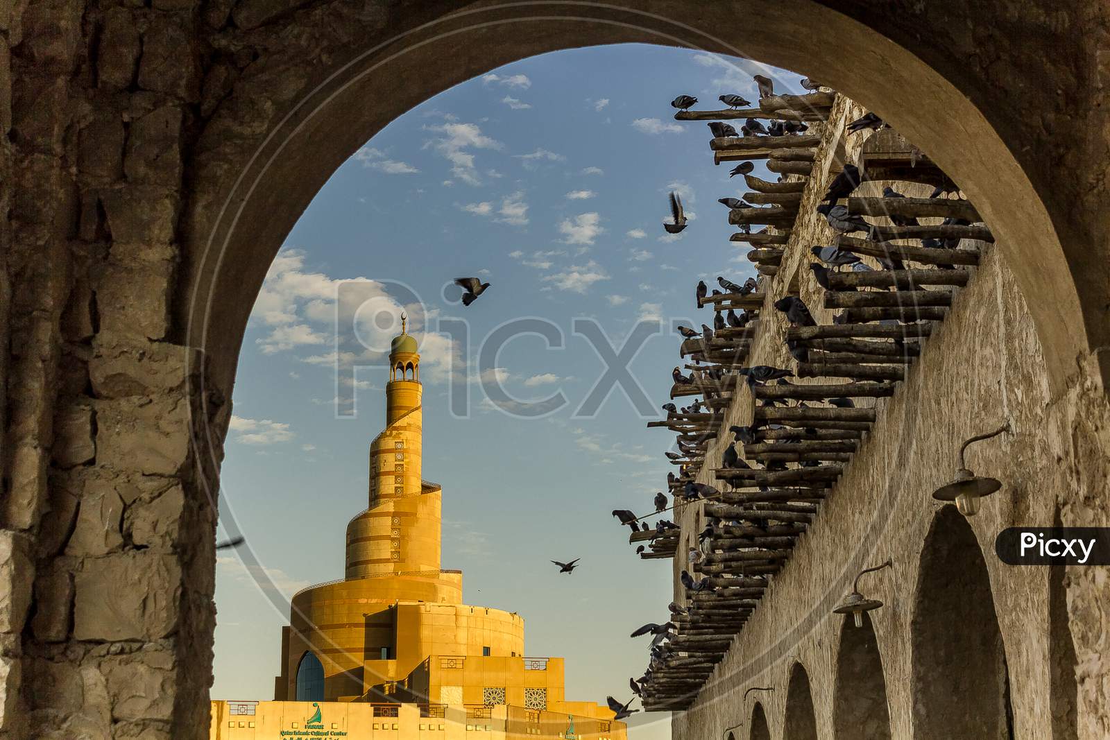 Al-Fanar Qatar Islamic Cultural Center daylight exterior view with pigeons flying in the sky in foreground and clouds in sky in background