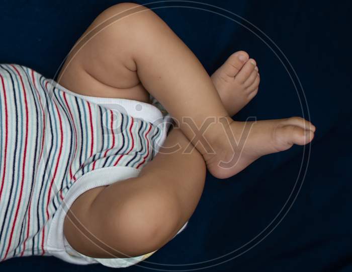Infant Legs On A Bed Sheet Of Blue Color