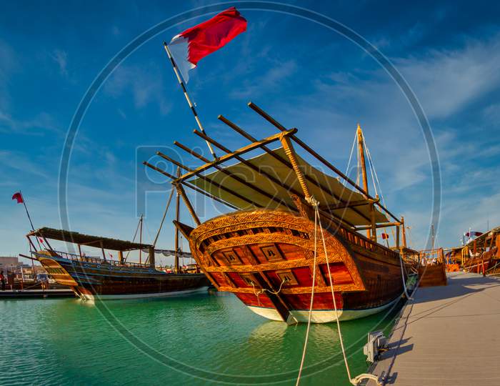 Traditional wooden boats (dhows) in Katara beach Qatar daylight view with Qatar flag and clouds in sky