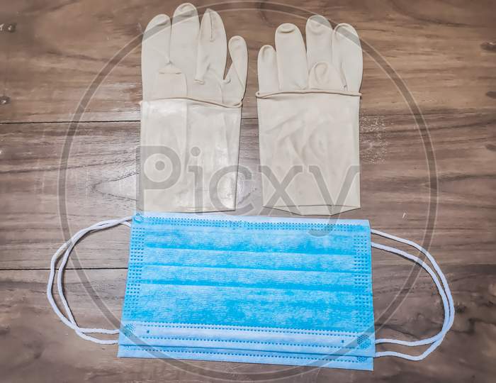 A Pair Of Rubber Medical Gloves, Surgical Mask On A Wooden Table