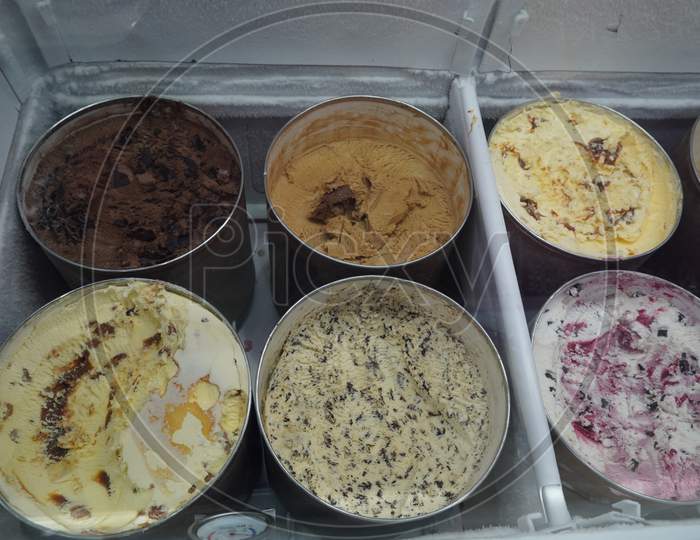 Bulk Ice Cream Kept In Large Round Containers Behind Glass At Gelato Shop. Ice Cream In A Candy Store. Pistachio, Chocolate, Strawberry, Banana Ice Cream Bar At All You Can Eat Buffet Restaurant.