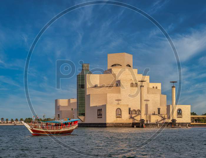Museum of Islamic Art ,Doha,Qatar in daylight exterior view with Arabic gulf and dhow in the foreground and clouds in sky