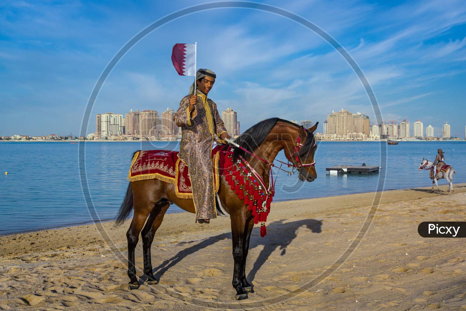 A Qatari man riding a horse and carry Qatar flag in Katara beach celebrating Qatar National Day