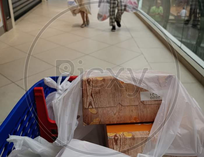 Corona virus safe shopping, the photo shows a shopping cart in the foreground and two walking women wearing medical masks and carrying shopping bags