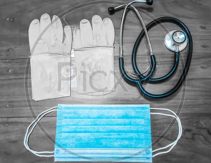 A Pair Of Rubber Medical Gloves, Surgical Mask And Black Stethoscope On A Wooden Table.