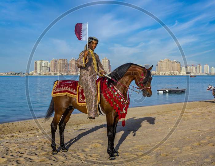 A Qatari man riding a horse and carry Qatar flag in Katara beach celebrating Qatar National Day