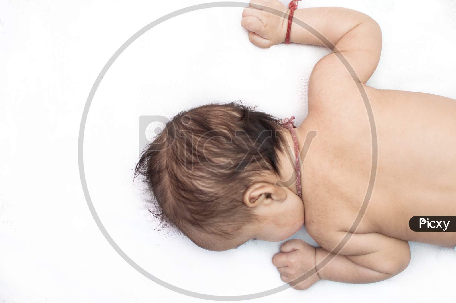 Small Baby Lying On A White Bed Sheet On His Chest Facing Left With Open Hands
