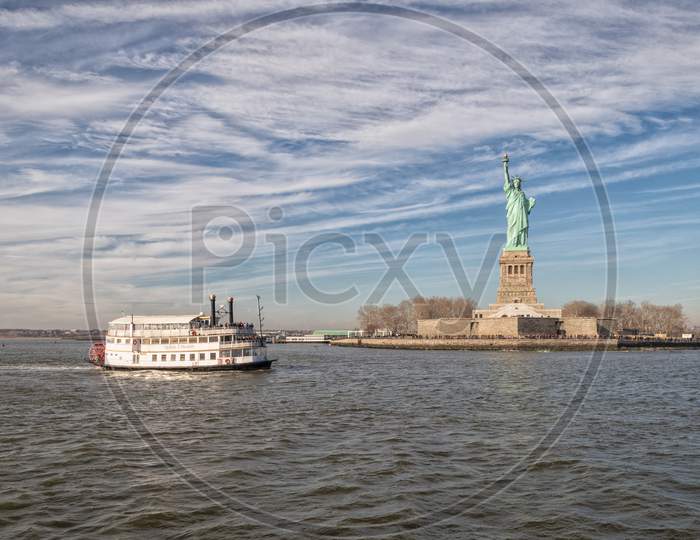 The Statue of Liberty in New York City USA daylight view with clouds in sky and ferry in river