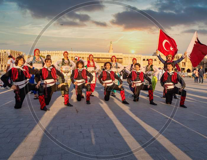 Turkish folklore dance group carrying Qatar and Turkish flags in Souk Waqif, Doha Qatar daylight view with clouds in sky in background