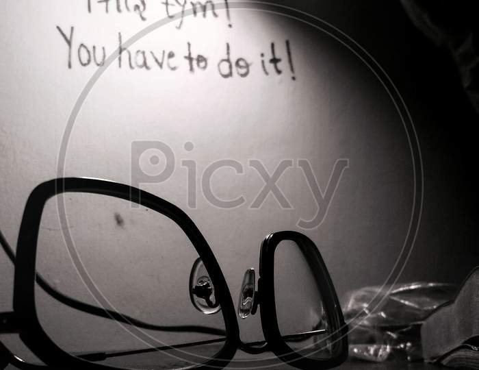 specs and lamp on a studying table and a motivational quote on the wall .