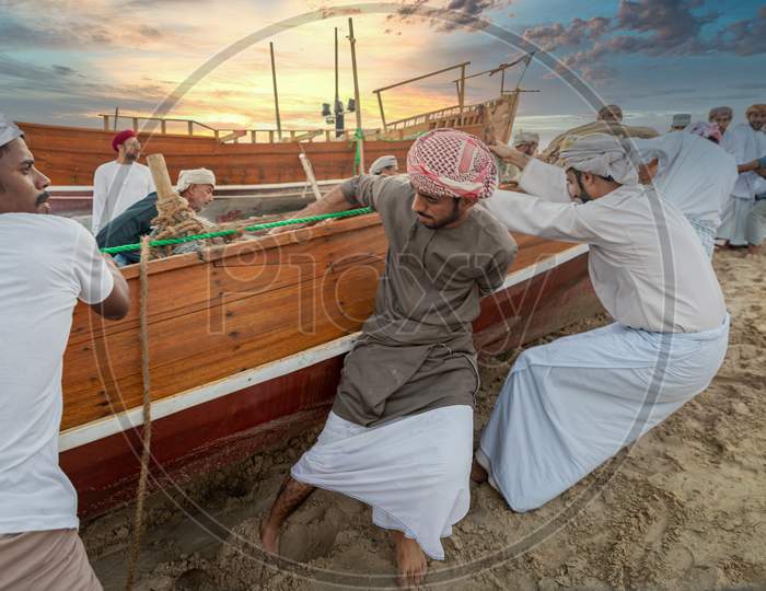 Traditional Arabic fishermen working  in Katara beach with dhows in the water and clouds in the sky in background.