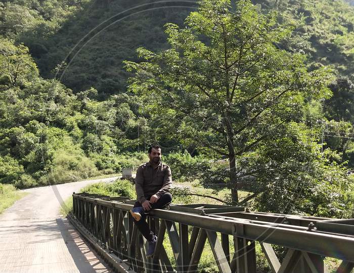 Man sitting on bridge with greenery