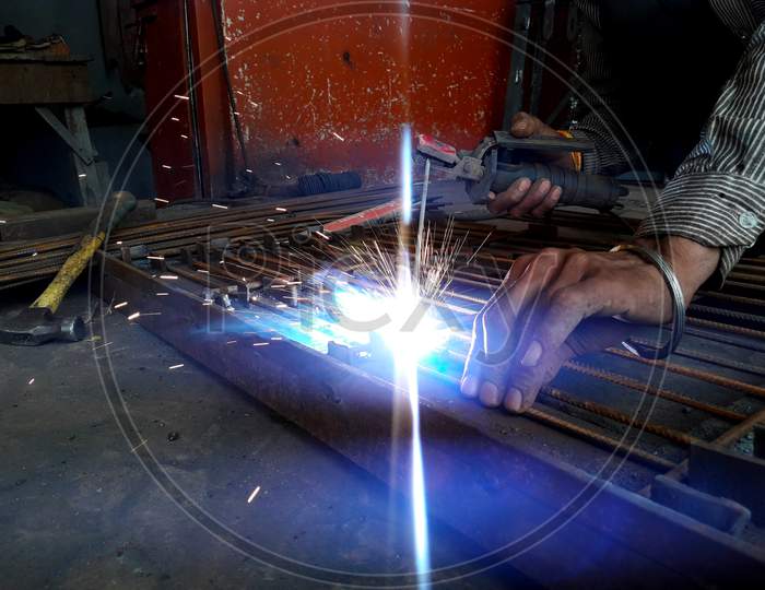 Generating Blue Sparks While Worker Welding On Iron In Industrial Workshop