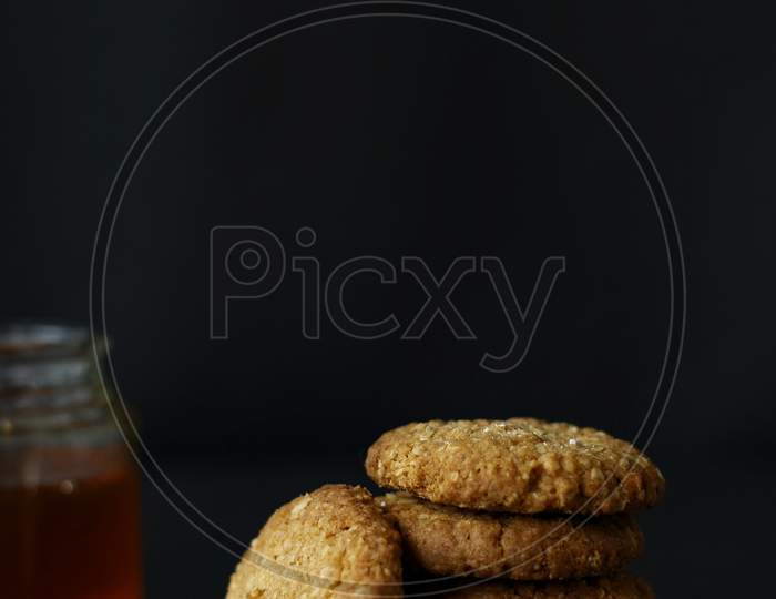 Honey And Oats Cookies Stacked On Each Other With Honey Pot On A Dark Background
