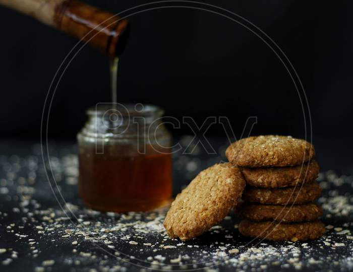 Honey And Oats Cookies Stacked On Each Other With Honey Pot On A Dark Background