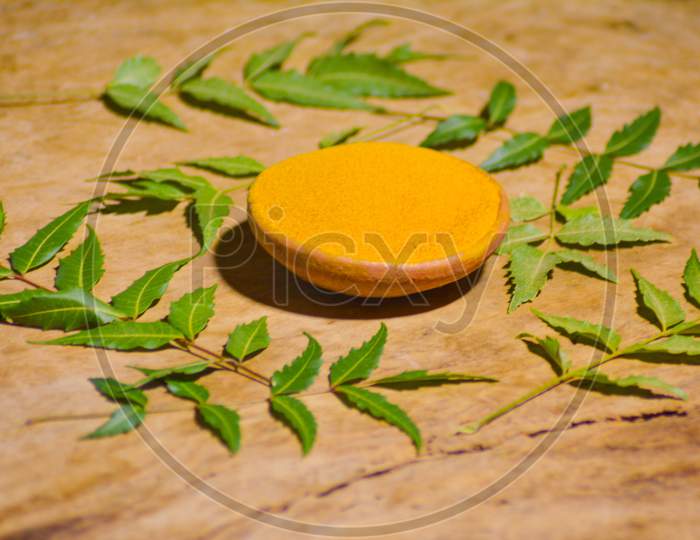 Medicinal turmeric powder with neem leaves over wood background