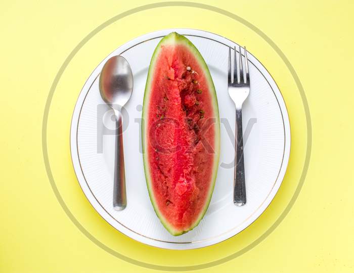 Sliced Watermelon on white plate with spoon and fork stock photo with yellow background.