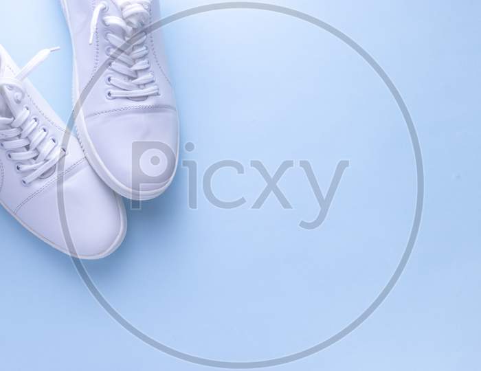 White sneakers on light blue colour background, flat lay top view minimal background.