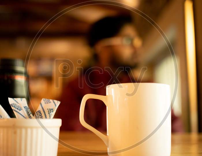 white Coffee cup with sugar pouch with person in background in cafe
