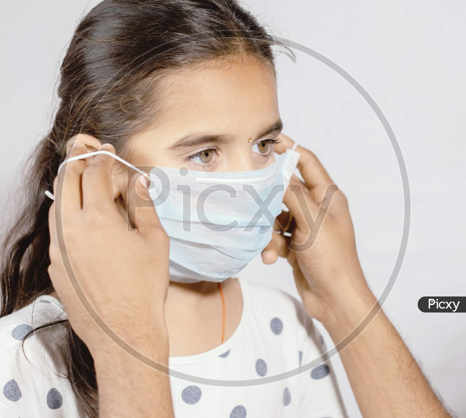 Prevention Of Spreading The Coronavirus Or Covid-19 Outbreak By Wearing Mask - Father Wearing A Disposable Hygienic Face Mask To His Young Girl Daughter To Protect Spread Of Disease.