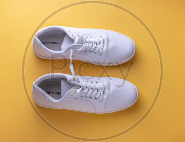 White sneakers on light yellow colour background, flat lay top view minimal background.