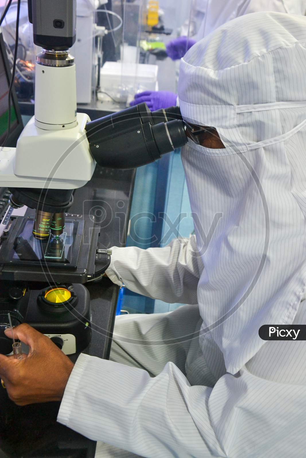 Scientist in protective coverall doing research and testing through microscope at a laboratory in India, while maintaining quality standards and protocols, PPE, personal protective equipment