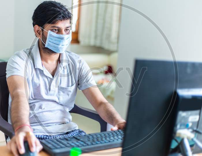 Young Man Quarantined At Home During World Pandemic Of Coronavirus Covid-19 Prevention. Stay At Home, Stay Safe. Man With Protective Medical Mask Using Computer. Isolation, Lock Down Situation.